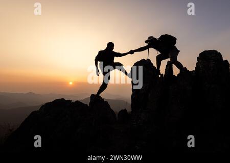 Person auf dem Gipfel des Berges. Silhouette des Personals, das bei Sonnenuntergang auf den Gipfel des Berges wandert, und das Klettern des Teams auf dem Berg. Führungskonzept, t Stockfoto