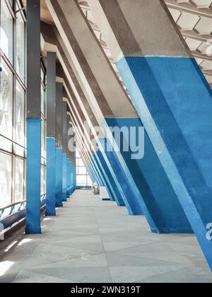 Säulen und Balken im Zhytniy Market - modernistische Markthalle. Geometrischer dreieckiger Durchgang entlang der Glaswand, schwindende Perspektive. Stockfoto