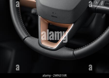 Untere Hälfte des Fahrzeuglenkrads mit Kupferelementen. Lederlenkrad mit beigefarbenen Nähten. Innenraum eines modernen Kompaktwagens. Stockfoto
