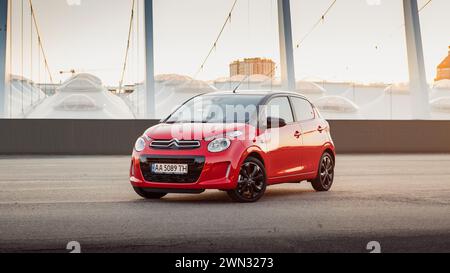 Red Citroen C1 vor dem modernen Stadion. Vorderansicht von drei Vierteln der kompakten roten französischen Fließhecke, die auf dem großen Asphaltfeld geparkt ist, mit Blick auf die Stadt Stockfoto