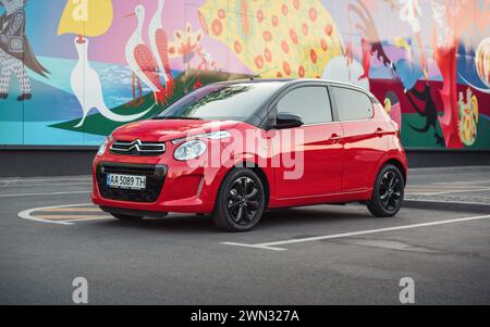 Rote Citroen C1 vor der farbenfrohen Wand. Vorderansicht von drei Vierteln mit kompaktem, rotem französischem Fließheck in urbaner Umgebung - geparkt in der Nähe der Mauer mit Volksmotiv Stockfoto