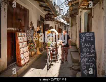 Ein Teehändler mit seinem Dreirad in einer Gasse neben einem Gewürzladen, Stone Town, Sansibar, Tansania Stockfoto