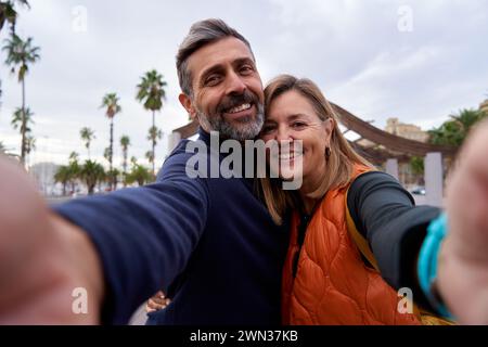 Glückliches Paar mittleren Alters, das Handy benutzt, um draußen ein Selfie zu machen. Stockfoto