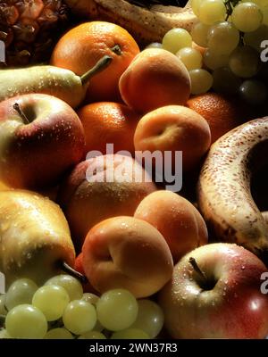 Ein lebhaftes Sortiment an frischen Früchten glitzert mit Feuchtigkeit: Äpfel, Orangen, Aprikosen, Trauben, Bananen, Birnen und vieles mehr, in dramatischer Beleuchtung getaucht. Stockfoto
