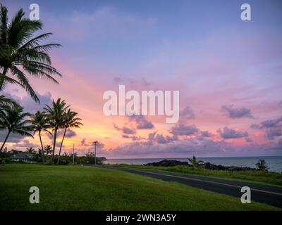 Eine malerische Küstenstraße bei Sonnenuntergang mit dem farbenfrohen Himmel über dem Meer und Palmen Stockfoto
