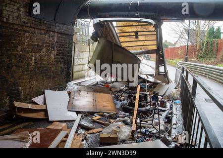 Slough, Berkshire, Großbritannien. Februar 2024. Ein Van ist in der Station Road in Slough nahe der Burnham Station auf die Eisenbahnbrücke gestoßen. Die Niederbrücke, die deutlich als Niederbrücke gekennzeichnet ist und ein blinkendes Schild zur Warnung von Fahrzeugen hat, liegt unterhalb der Eisenbahnlinie, die von Elizabeth Line und GWR-Zügen genutzt wird. Die Züge fahren jedoch noch. Das Fahrerhaus wurde weggefahren und der Inhalt, der wie Baumüll aussieht, wurde verstreut in der Brücke zurückgelassen. Der Van hat ein Logo für Lambournes, 24-Stunden-Hecklift und Shutter-Reparaturen auf der Rückseite. Die Straße ist Stockfoto