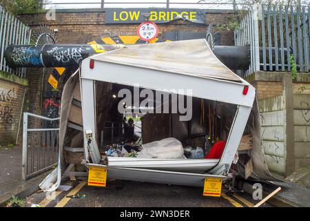 Slough, Berkshire, Großbritannien. Februar 2024. Ein Van ist in der Station Road in Slough nahe der Burnham Station auf die Eisenbahnbrücke gestoßen. Die Niederbrücke, die deutlich als Niederbrücke gekennzeichnet ist und ein blinkendes Schild zur Warnung von Fahrzeugen hat, liegt unterhalb der Eisenbahnlinie, die von Elizabeth Line und GWR-Zügen genutzt wird. Die Züge fahren jedoch noch. Das Fahrerhaus wurde weggefahren und der Inhalt, der wie Baumüll aussieht, wurde verstreut in der Brücke zurückgelassen. Der Van hat ein Logo für Lambournes, 24-Stunden-Hecklift und Shutter-Reparaturen auf der Rückseite. Die Straße ist Stockfoto