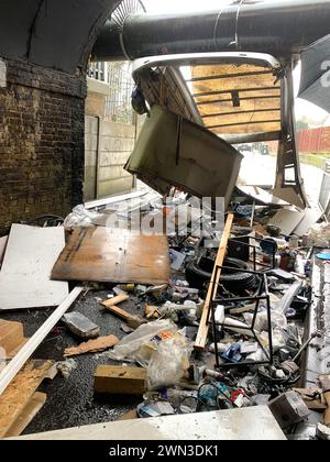 Slough, Berkshire, Großbritannien. Februar 2024. Ein Van ist in der Station Road in Slough nahe der Burnham Station auf die Eisenbahnbrücke gestoßen. Die Niederbrücke, die deutlich als Niederbrücke gekennzeichnet ist und ein blinkendes Schild zur Warnung von Fahrzeugen hat, liegt unterhalb der Eisenbahnlinie, die von Elizabeth Line und GWR-Zügen genutzt wird. Die Züge fahren jedoch noch. Das Fahrerhaus wurde weggefahren und der Inhalt, der wie Baumüll aussieht, wurde verstreut in der Brücke zurückgelassen. Der Van hat ein Logo für Lambournes, 24-Stunden-Hecklift und Shutter-Reparaturen auf der Rückseite. Die Straße ist Stockfoto