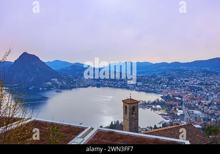 Das Bergdorf Aldesago öffnet den Blick auf den spiegelartigen Luganer See und den Monte San Salvatore vor dem violetten Abendhimmel, Lugano, Tessin Stockfoto