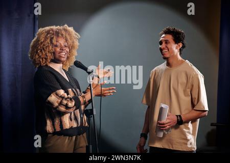 Junge fröhliche Afroamerikanerin, die das Publikum präsentiert, neuen männlichen Comedian des Stand Up Clubs und spricht im Mikrofon Stockfoto