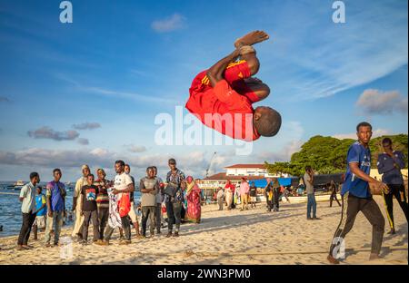 Ein junger Mann spielt Akrobatik am späten Nachmittag am Strand in Stone Town, Sansibar, Tansania. Stockfoto