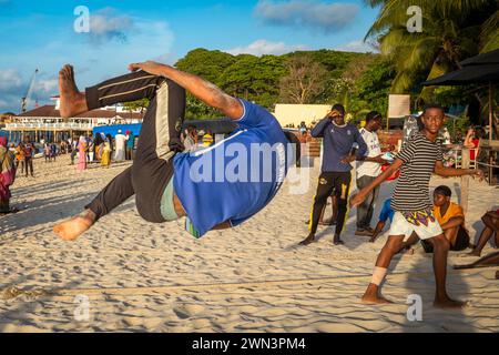 Ein junger Mann spielt Akrobatik am späten Nachmittag am Strand in Stone Town, Sansibar, Tansania. Stockfoto