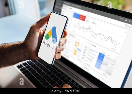 Mann, der ein Mobiltelefon mit Google Ads auf dem Bildschirm und im Hintergrund einen Computer mit Anzeigenstatistiken verwendet. Stockfoto