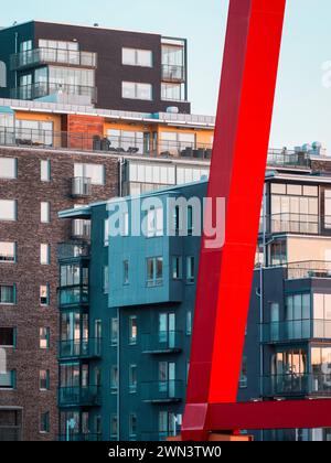 Ein leuchtend rotes architektonisches Element zieht sich durch die Szene und kontrastiert mit den modernen blauen und grauen Wohnhäusern von Göteborg, Schweden. T Stockfoto