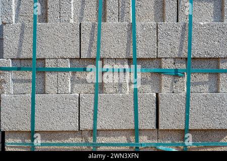 Grauer Zement-Schlackenblock, der übereinander steht und auf der Baustelle mit Streifen gebunden ist Stockfoto