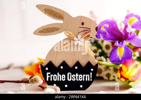 Augsburg, Bayern, Deutschland - 28. Februar 2024: Happy Easter Greeting auf einem hölzernen Osterhasen neben einem bunten Blumenstrauß. FOTOMONTAGE *** Frohe Ostern Gruß auf einem Holz Osterhasen neben einem bunten Blumenstrauß. FOTOMONTAGE Stockfoto