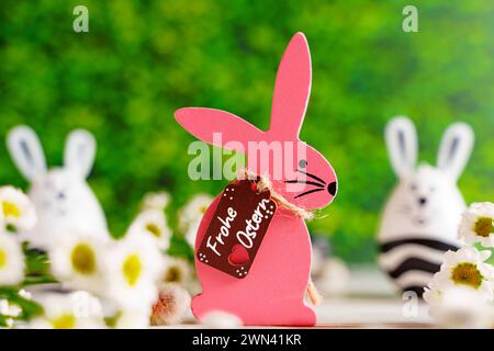 Augsburg, Bayern, Deutschland - 28. Februar 2024: Frohe Ostergrüße auf einem rosa hölzernen Osterhasen neben Blumen Dekoration *** Frohe Ostern Ostergrüße auf einem Pinken Osterhasen aus Holz neben Blumen Dekoration Stockfoto