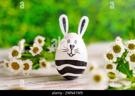 Augsburg, Bayern, Deutschland - 28. Februar 2024: Osterhasenei neben Blumenschmuck. Ostersymbolbild *** Osterhase EI neben Blumen Dekoration. Oster-Symbolbild Stockfoto