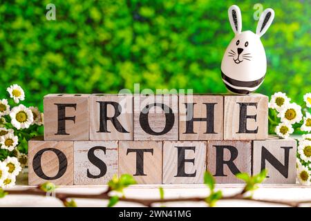 Augsburg, Bayern, Deutschland - 28. Februar 2024: Happy Easter geschrieben mit Holzwürfeln, Osterhasen-Ei und Frühlingsblumen. Ostersymbolbild *** Frohe Ostern schreibt mit Holzwürfeln, Osterhasen EI und frühlings Blumen. Oster-Symbolbild Stockfoto