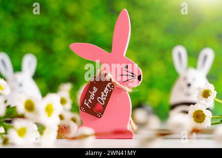 Augsburg, Bayern, Deutschland - 28. Februar 2024: Frohe Ostergrüße auf einem rosa hölzernen Osterhasen neben Blumen Dekoration *** Frohe Ostern Ostergrüße auf einem Pinken Osterhasen aus Holz neben Blumen Dekoration Stockfoto