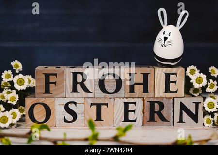 Augsburg, Bayern, Deutschland - 28. Februar 2024: Happy Easter geschrieben mit Holzwürfeln, Osterhasen-Ei und Frühlingsblumen. Ostersymbolbild *** Frohe Ostern schreibt mit Holzwürfeln, Osterhasen EI und frühlings Blumen. Oster-Symbolbild Stockfoto