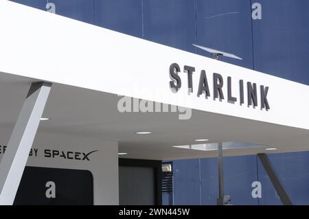 Barcelona, Spanien. Februar 2024. Das Logo des Starlink-Satellitennetzes, das von der Luft- und Raumfahrtgesellschaft SpaceX betrieben wird, ist im Marketing-Pavillon auf der Messe Mobile World Congress (MWC) in Barcelona zu sehen. Auf dem Dach über dem Logo ist ein Starlink-Empfänger zu sehen. Quelle: Wolf von Dewitz/dpa-Zentralbild/dpa/Alamy Live News Stockfoto