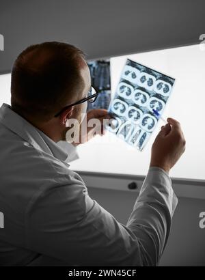 Rückansicht des Arztes, der MRT-Ergebnisse untersucht. Der in der Klinik tätige Facharzt führt die Beschreibung von Röntgenaufnahmen des Patienten durch. Konzept der modernen Diagnostik. Stockfoto