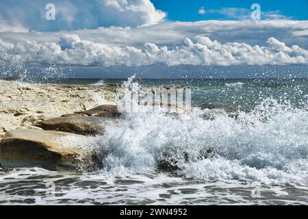 Wellen brechen an einer felsigen Küste ab. Beeindruckende Wolkenlandschaft mit bedrohlichen Gewitterwolken und blauem Himmel. Südküste Zyperns. Stockfoto