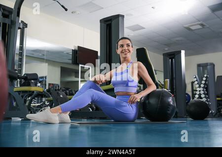 Sportliche Frau mit Medizinball auf dem Boden im modernen Fitnessstudio Stockfoto