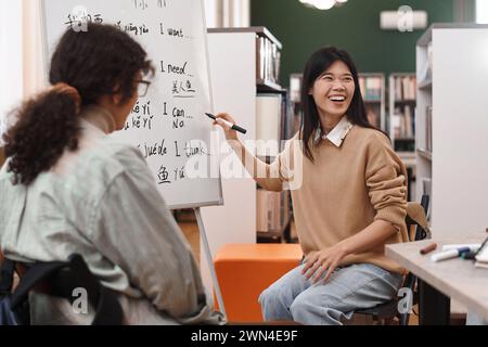 Porträt einer jungen asiatischen Frau, die fröhlich auf das Whiteboard mit Hieroglyphen zeigt und Spaß am Chinesischen Sprachunterricht hat Stockfoto