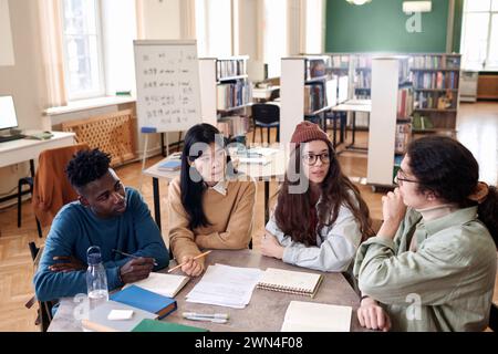 Hochwinkelansicht bei einer internationalen Gruppe von Studenten, die das Projekt diskutieren, am Tisch in der Universitätsbibliothek sitzen und Ideen im Kopierbereich präsentieren Stockfoto