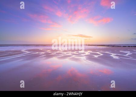 Ein Himmel voller Sonnenuntergang spiegelt sich auf dem nassen Sand des Zoutelande Strandes während eines beruhigenden Sonnenuntergangs an einem ruhigen und schönen Abend, das Wasser fließt. Stockfoto