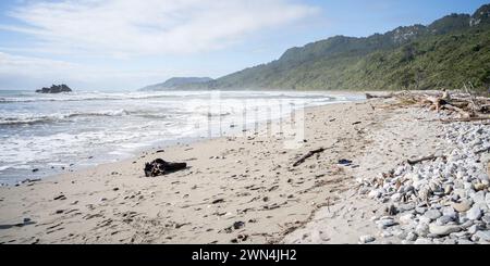 Mann am Rande eines rauen, einsamen Strandes mit Regenwald im Hintergrund, Neuseeland Stockfoto