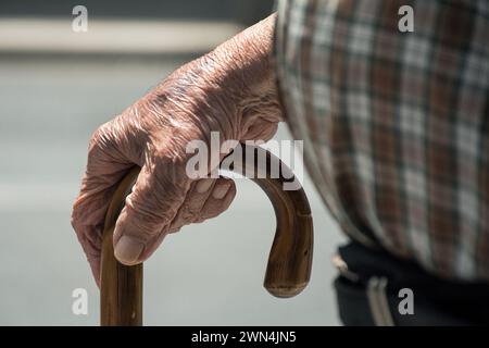 Nahaufnahme der zerknitterten, alten Hand eines älteren Mannes, der den gebogenen Holzgriff eines Rohrs ergreift. Stockfoto