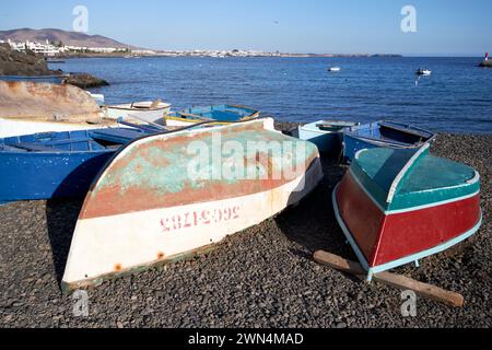 Umgestürzt gelagerte lokale kleine Fischerruderboote am Steinstrand in der Nähe des Hafens playa blanca, Lanzarote, Kanarische Inseln, spanien Stockfoto