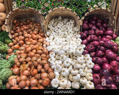 Knoblauch, weiße Zwiebeln, rote Zwiebeln und Artischocken, die in Korbkörben in Supermärkten verkauft werden Stockfoto