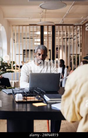 Geschäftsmann, der am Laptop arbeitet, während er im Coworking-Büro am Schreibtisch sitzt Stockfoto