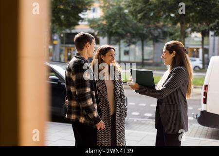 Lächelnde Verkäuferin, die mit einem Paar spricht, während sie auf der Straße steht Stockfoto