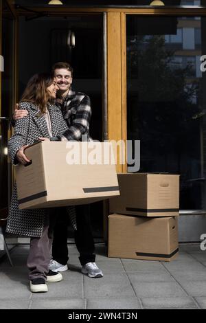 Lächelnder Mann, der eine Frau umschließt, während er vor der Wohnung steht Stockfoto