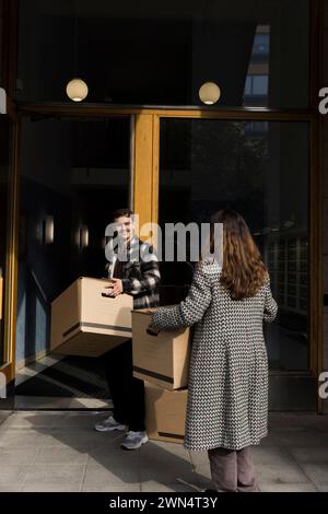 Ein Mann hilft der Frau, während er Pappkartons in der Nähe des Wohngebäudes trägt Stockfoto