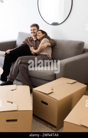 Glückliches Paar, das sich umschließt, während es zu Hause auf dem Sofa neben Pappkartons sitzt Stockfoto
