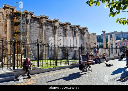 Athen, Griechenland - 19. Dezember 2023: Nicht identifizierte Menschen und Straßenmusiker mit Gitarre und traditionellem Bouzouki, Hadrians Bibliothek im Hintergrund Stockfoto