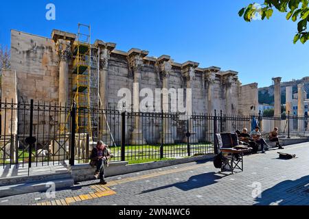 Athen, Griechenland - 19. Dezember 2023: Nicht identifizierte Menschen und Straßenmusiker mit Gitarre und traditionellem Bouzouki, Hadrians Bibliothek im Hintergrund Stockfoto