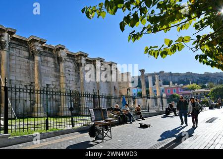 Athen, Griechenland - 19. Dezember 2023: Nicht identifizierte Menschen und Straßenmusiker mit Gitarre und traditionellem Bouzouki, Hadrians Bibliothek im Hintergrund Stockfoto