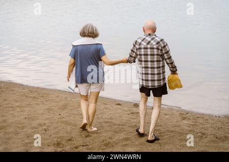 Rückansicht eines älteren Ehepaares, das Hände hält, während er in Richtung Fluss geht Stockfoto