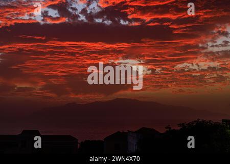 Die Sonne untergeht hinter der Silhouette von ilha brava und beleuchtet die Unterseite von schweren niedrigen Wolken in leuchtendem Rot mit der fogo-Insel im Vordergrund in kap verde Stockfoto