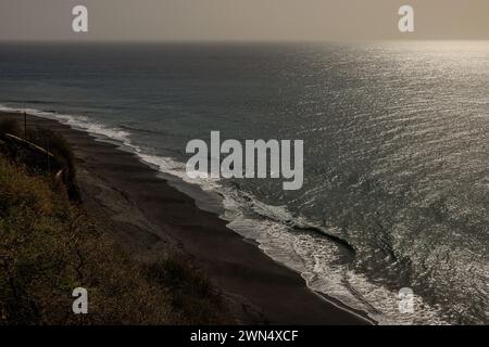 Weite Aussicht auf das ruhige Meer und sanfte Wellen, die am langen schwarzen Vulkanstrand brechen, und die niedrige Sonne auf der Insel praia de fonte Bila sao filipe fogo kap verde Stockfoto