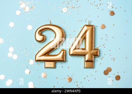 24 Jahre Feier. Begrüßungsbanner. Goldkerzen in Form von Nummer 24 auf pfirsichfarbenem Hintergrund mit Konfetti. Stockfoto