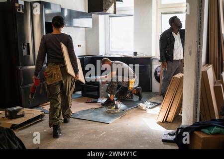 Zimmerfrau mit Planke, während Kollegen in der Küche vor Ort arbeiten Stockfoto