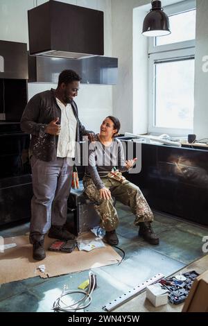 Fröhliche, multirassische Zimmerleute diskutieren gemeinsam in der Küche der Wohnung Stockfoto